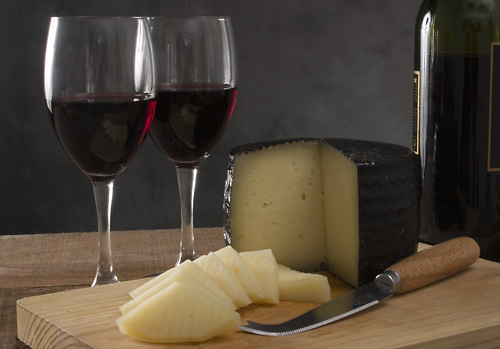 cheese and wine placed on wooden cutting board